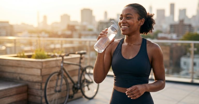A woman sips water on a sunny rooftop after her run, considering when plain fluids are enough and when IV hydration might help more.